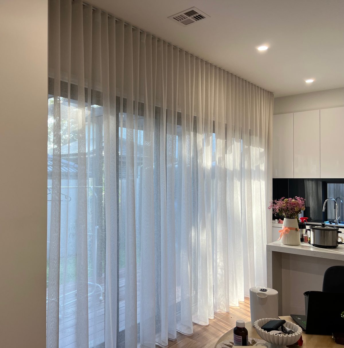 White wave fold sheers running floor to ceiling across glass doors beside a white kitchen