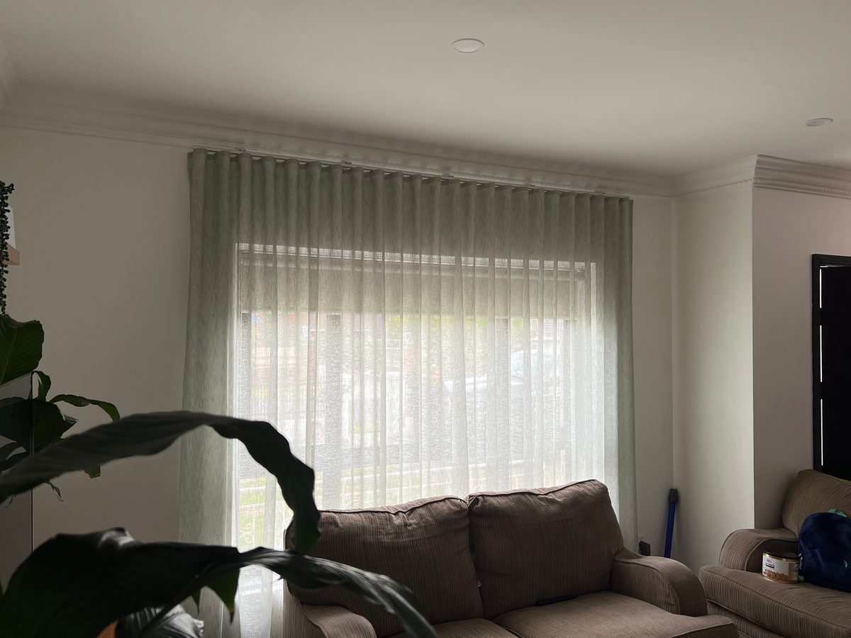 Soft green wave fold sheers across a living room window behind a grey couch