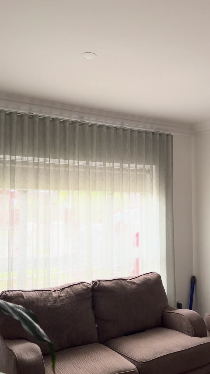 Wave fold sheer curtains across a living room window behind a grey couch