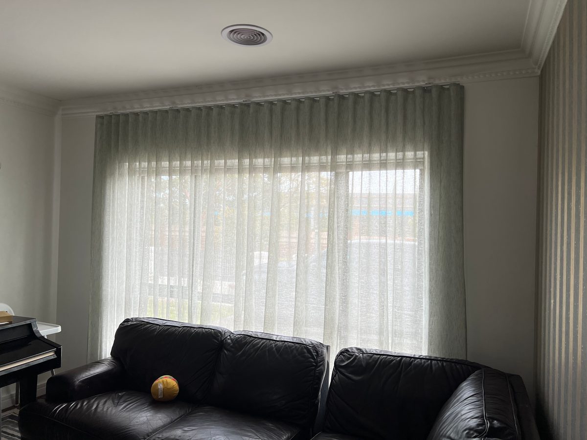 Soft green wave fold sheers across a wide lounge window behind a black leather couch